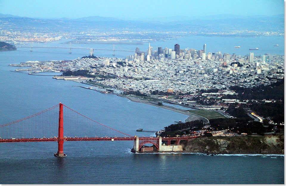 Rundflug ber San Francisco. Im Vordergrund die Golden Gate Bridge, dahinter der Hafen und die Shyline und links hinten die San Francisco-Oakland Bay Bridge.