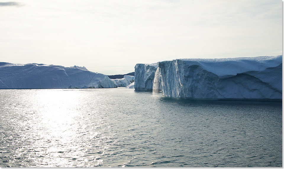 Die warmen Sonnenstrahlen schmelzen die Oberflächen der Eisberge ab. Das Schmelzwasser stürzt hier in einem Wasserfall in die See