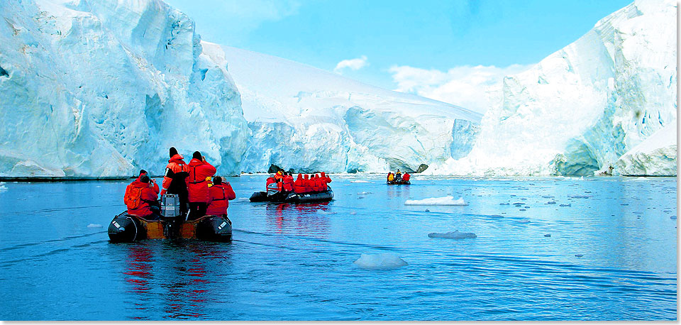 In rote Daunenjacken gepackt bewegt sich eine Gruppe auf stark motorisierten Zodiacs auf die Eisberge Grönlands zu.