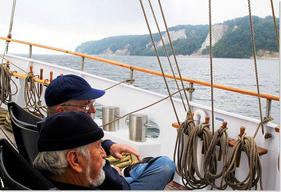 Zwei Männer in Betrachtung von Rügens Kreideküste an Steuerbord voraus.