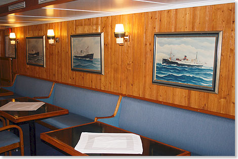 Die Cafeteria der LOFOTEN gefällt mit ihren holzgetäfelten Wänden und der Galerie historischer Hurtigruten-Schiffe an der Wand. 