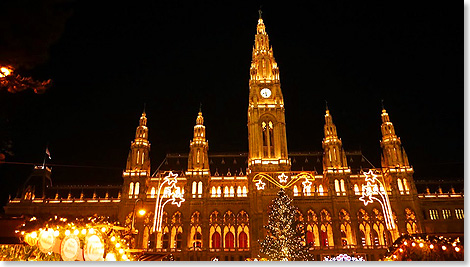 Das Rathaus ist hell erleuchtet hinter dem Christkindelmarkt.