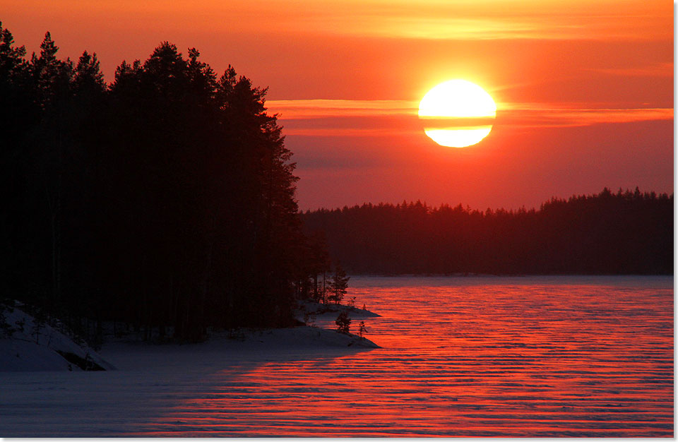 Der Sonnenuntergang lässt den Schnee auf dem Eis des Sees rot glühen.